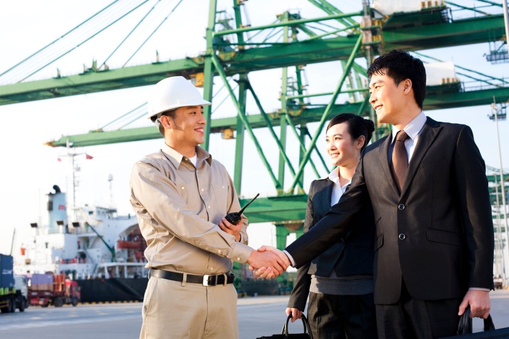 businesspeople and a shipping industry worker shaking hands at a shipping port